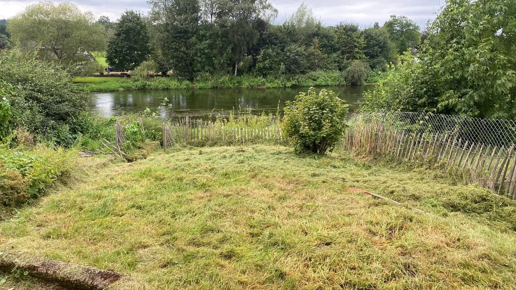 La pelouse tondue du jardin de Laiche, avec une clôture de châtaignier devant la rivière